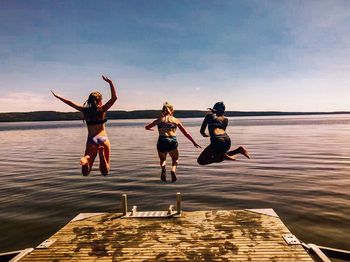 Rear view of female friends jumping in lake against sky