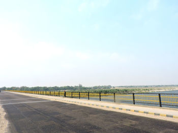 Empty road amidst field against sky