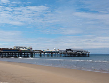 Pier on beach by sea against sky