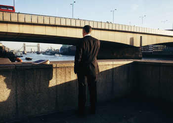 Rear view of man standing by railing against river