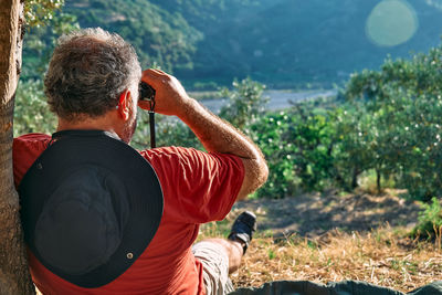 Rear view of tourist man looking through binoculars at the mountains view. hiking, unity with nature