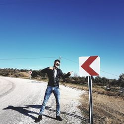 Full length portrait of man standing on road against clear blue sky