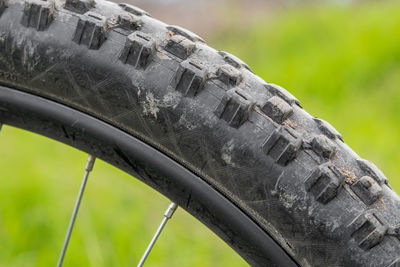 Part of a mountain bike wheel with a studded, slightly dirty tire. on a blurry green background