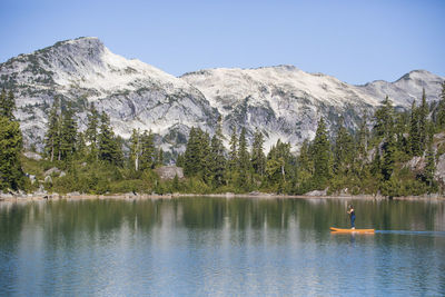 Side view of active woman paddle boarding on mountain lake.