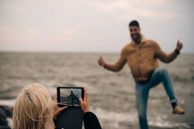 Young woman photographing man on digital tablet at beach