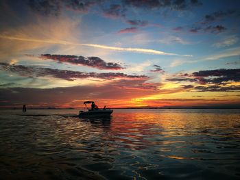 Silhouette man in sea against sky during sunset