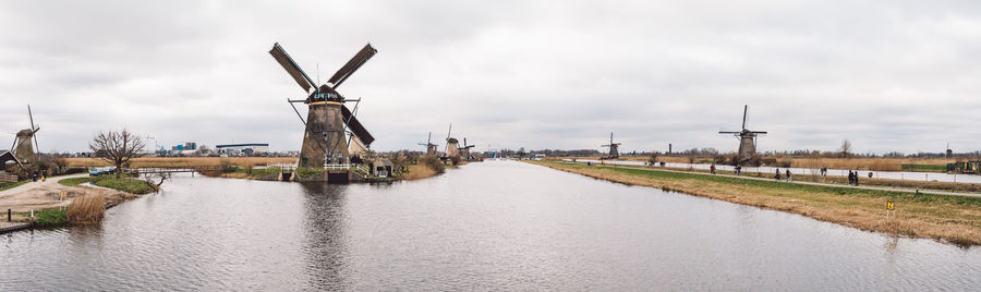 Traditional windmill by canal against sky