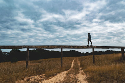 Woman standing on railing against sky