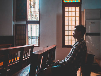 Side view of man praying while sitting on table at church