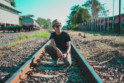 Full length of young man crouching on railroad track against sky
