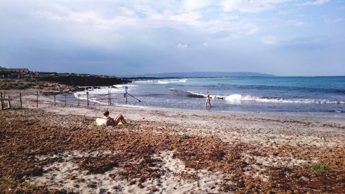 Woman relaxing at beach against cloudy sky