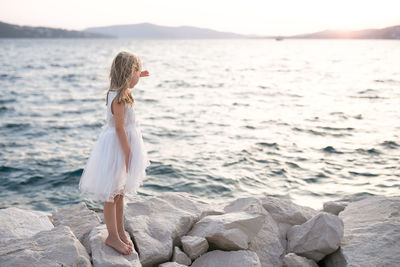 Side view of girl standing on rock by sea