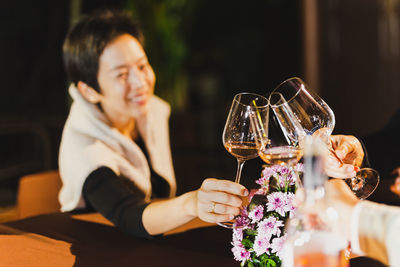 Happy woman clinking glass of wine with family sitting at dinner table.