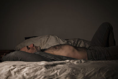 Adult man in open shirt and jeans lying on bed