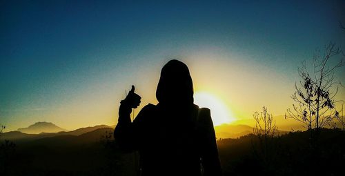 Silhouette woman using smart phone against sky at sunset