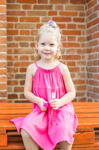 Portrait of cute girl sitting against brick wall