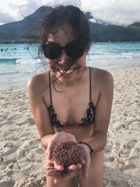 Portrait of young woman wearing bikini and sunglasses kneeling at beach