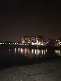 Illuminated cityscape by river against sky at night