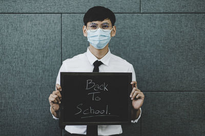 Portrait of man wearing flu mask holding slate against wall
