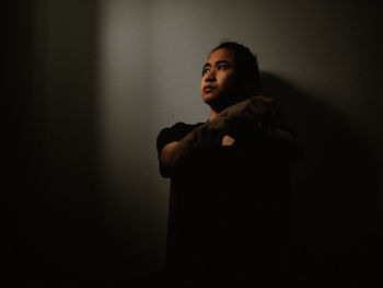 Young woman looking away while standing against black background