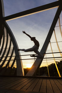 Side view of shirtless man jumping on footbridge during sunset