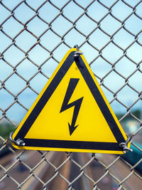 Yellow sign with lightning in triangle. the sign is hanging on the fence of a chain-link netting