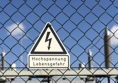 Close-up of information sign on chainlink fence against sky