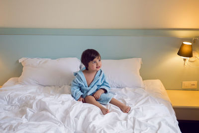 Baby boy two years old in a blue terry robe with a hood lying on a big bed