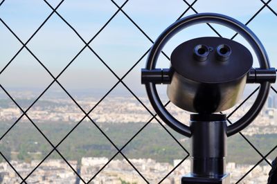 Coin-operated binoculars by fence at eiffel tower against sky