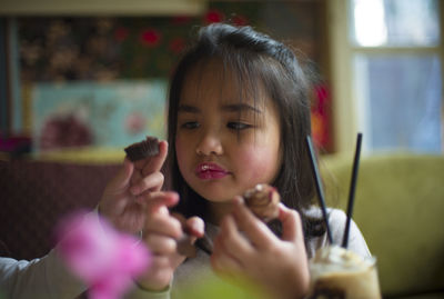 Cropped image of girl hand with sister eating cupcakes at home