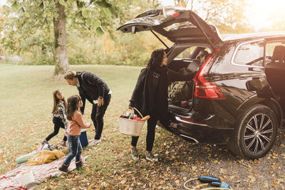 Family unloading luggage from electric car on field during picnic