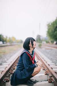 Woman looking away while sitting on railroad track against clear sky