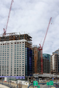 Low angle view of crane by buildings against sky