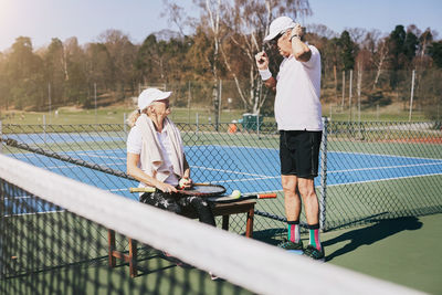 Senior man talking to friend at tennis court in summer