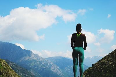 Rear view of young woman standing on mountain against sky