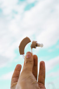 Cropped hands of person holding hearing aid against sky