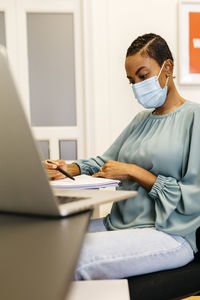 African businesswoman with safety mask reading papers while sitting in office