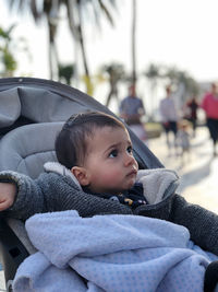 Little boy in his baby carriage, looking around, serious on a winter day. with a blanket on her lap. 