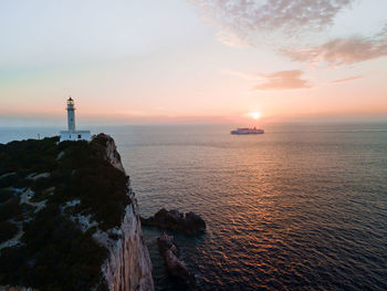 Lighthouse by sea against sky during sunset