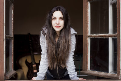 Portrait of young woman standing against window at home