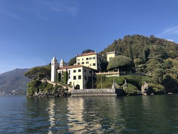 Lake by buildings against clear blue sky