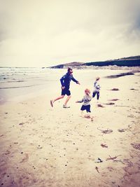 Father and children playing at beach against sky