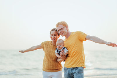 Full length of father and daughter standing at sea shore against clear sky