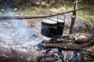 Close-up of containers hanging over bonfire in forest