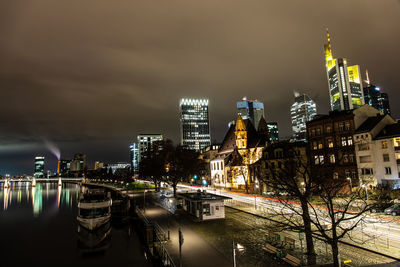 Illuminated buildings by street against sky at night