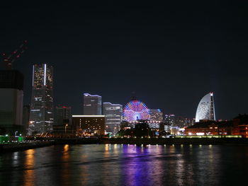 Illuminated buildings by river against sky at night