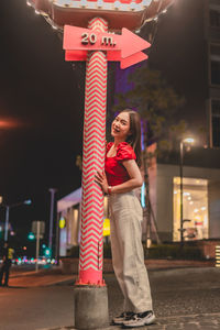 Portrait of woman standing on illuminated street in city at night