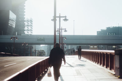 Rear view of man walking in city against clear sky