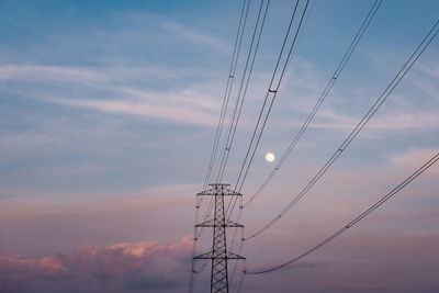 Low angle view of electricity pylon against sky during sunset with moon