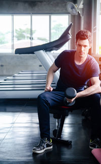 Thoughtful young man exercising with dumbbell in gym